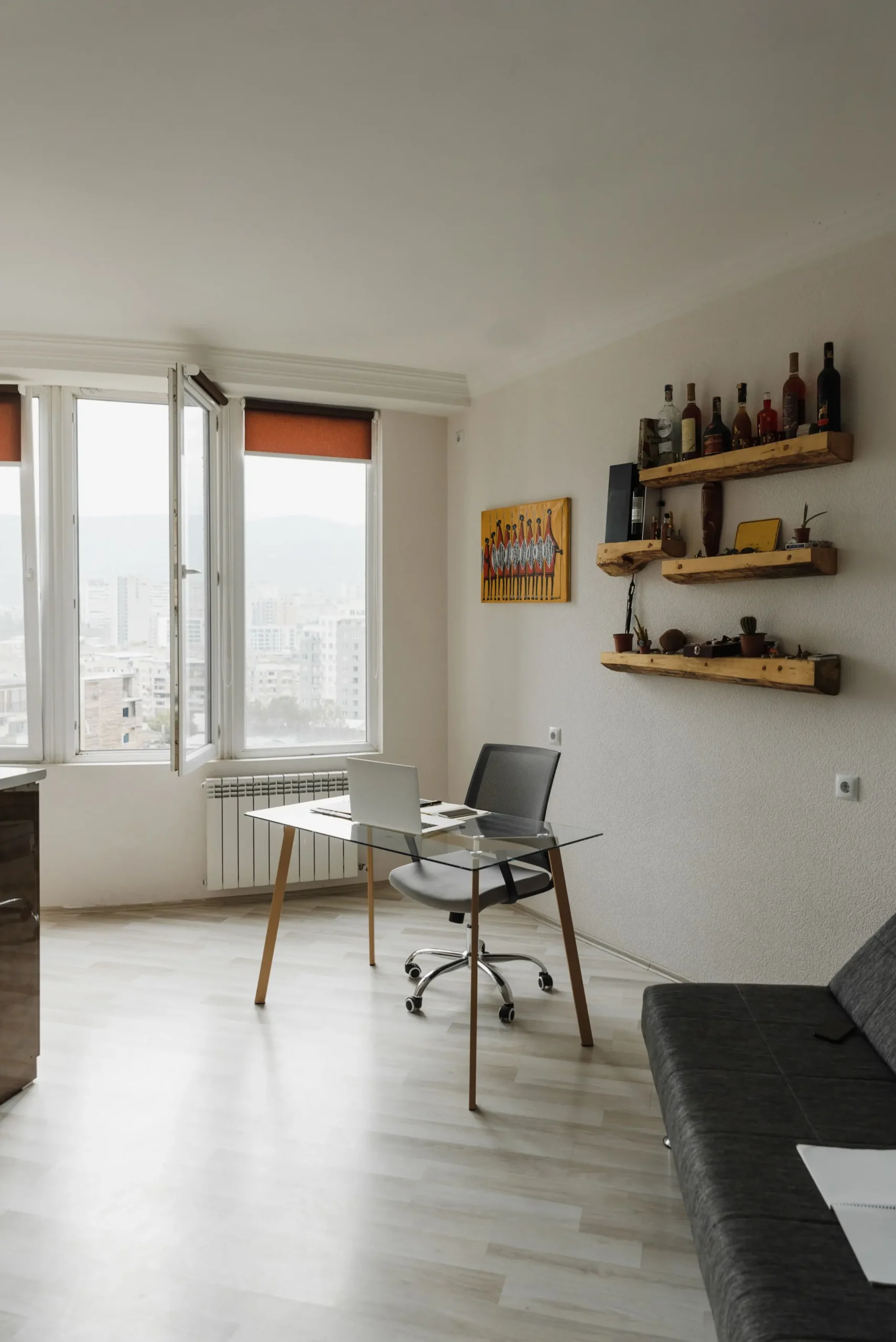Espacio de trabajo o estudio con escritorio de cristal, ordenador portátil, ventana exterior y estanterías de madera para vende piso Poblenou con Don Casa Inmobiliaria.
