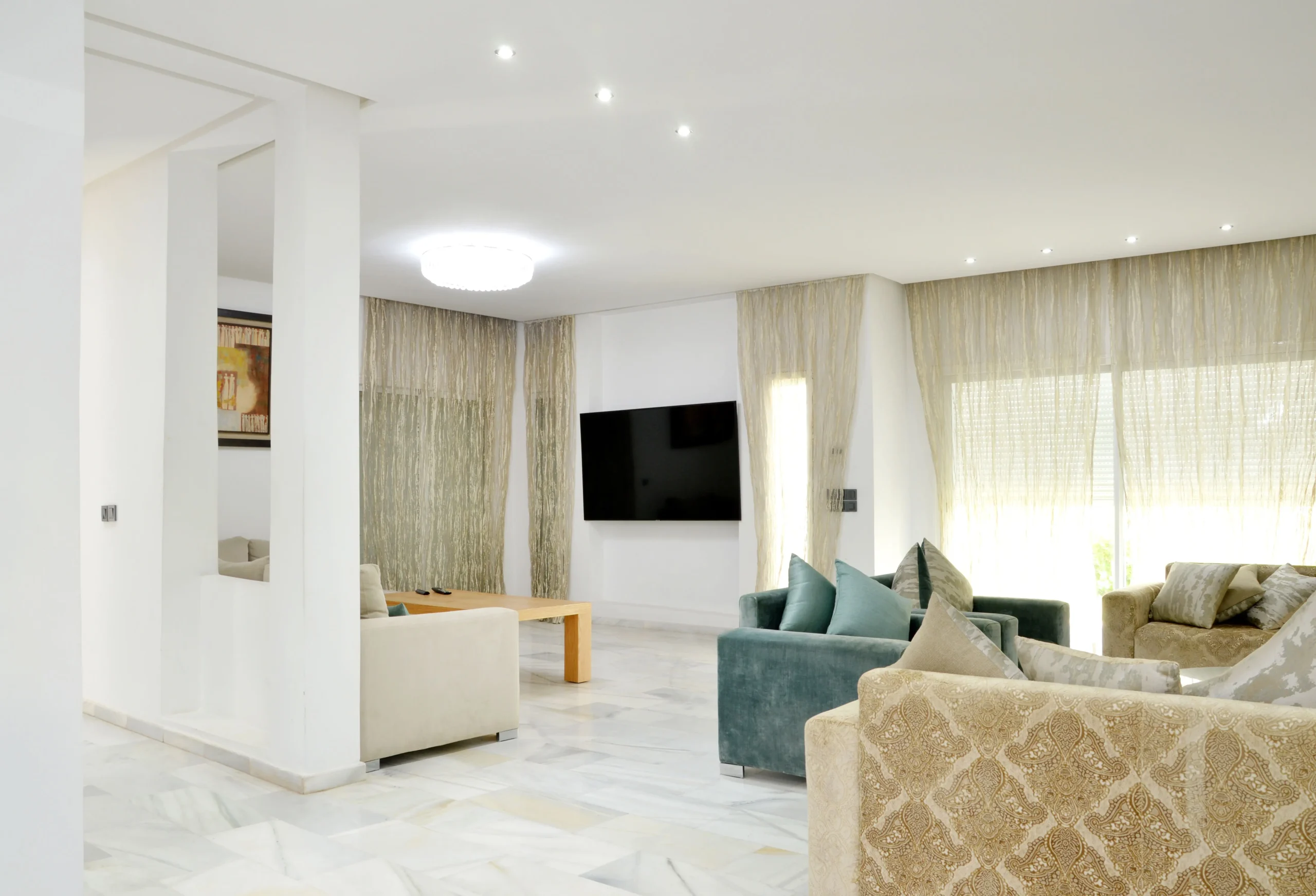 Espacioso salón de piso con suelo de mármol, sofás beige y verdes, gran televisión de pared y ventanales para vende piso Sants con Don Casa Inmobiliaria.