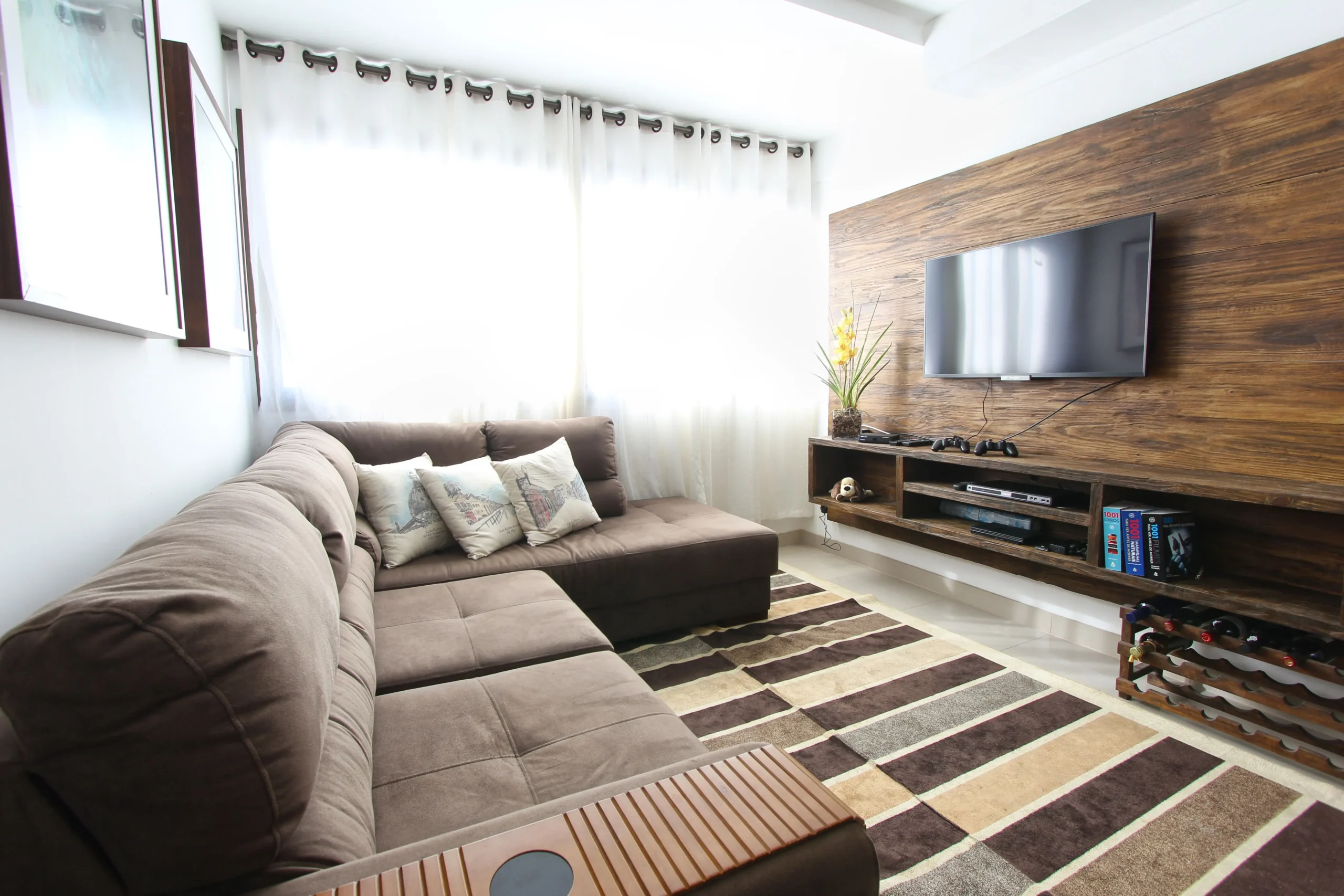 Salón de estar acogedor con gran sofá rinconero marrón, televisión sobre panel de madera natural y alfombra para vende piso Les Corts con Don Casa Inmobiliaria.