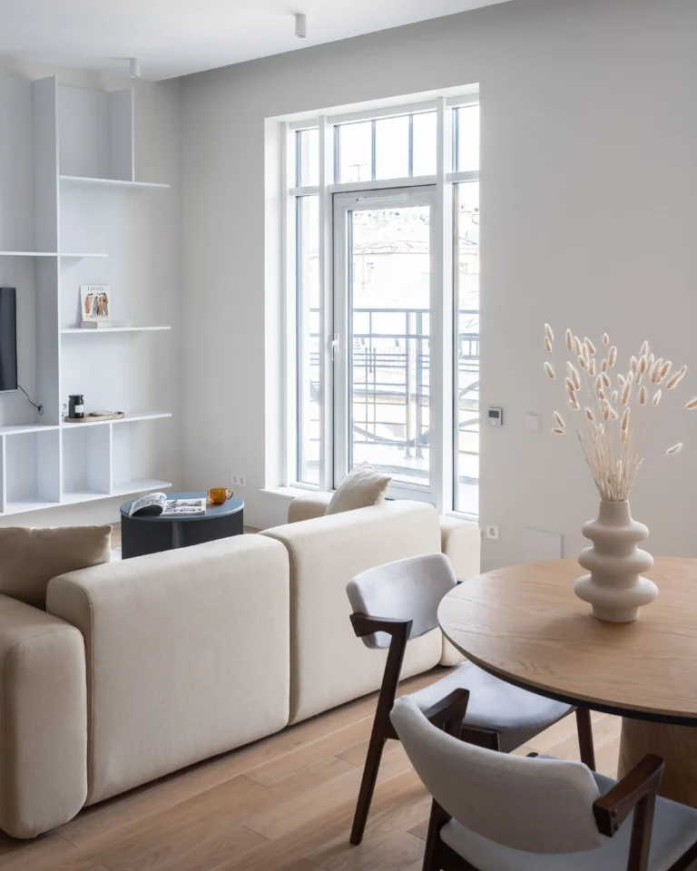 Interiorismo moderno y luminoso con sofá modular beige, mesa de comedor redonda de madera y ventanal balconero para vende piso Poblenou con Don Casa Inmobiliaria.